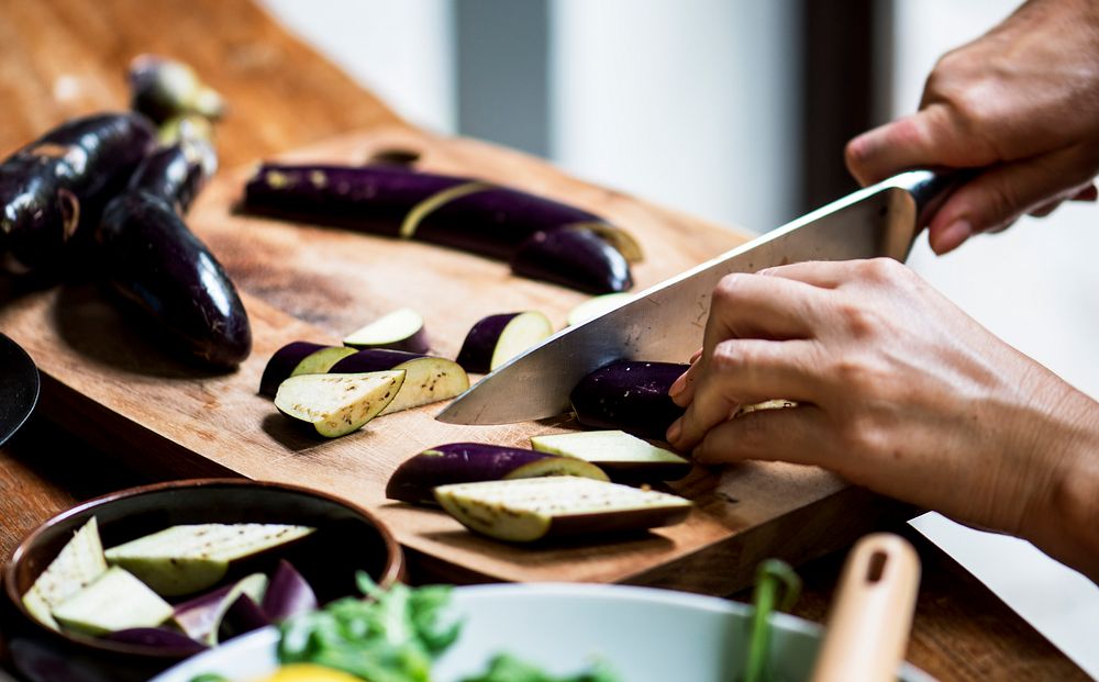 Closeup of hand with knife cutting eggplant