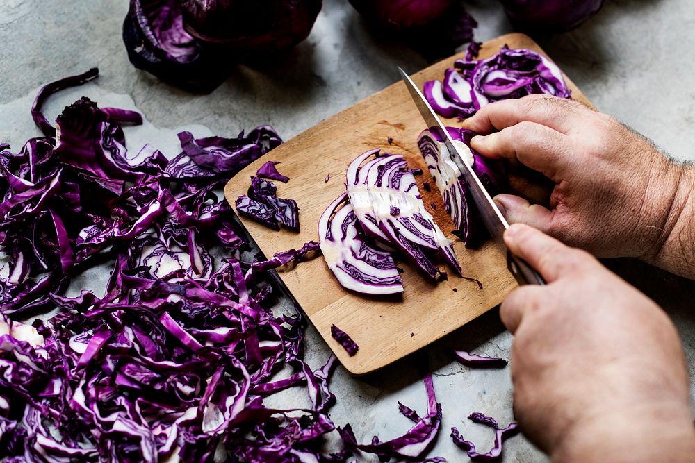 Closeup of hands with knife cutting red cabbage on cut board