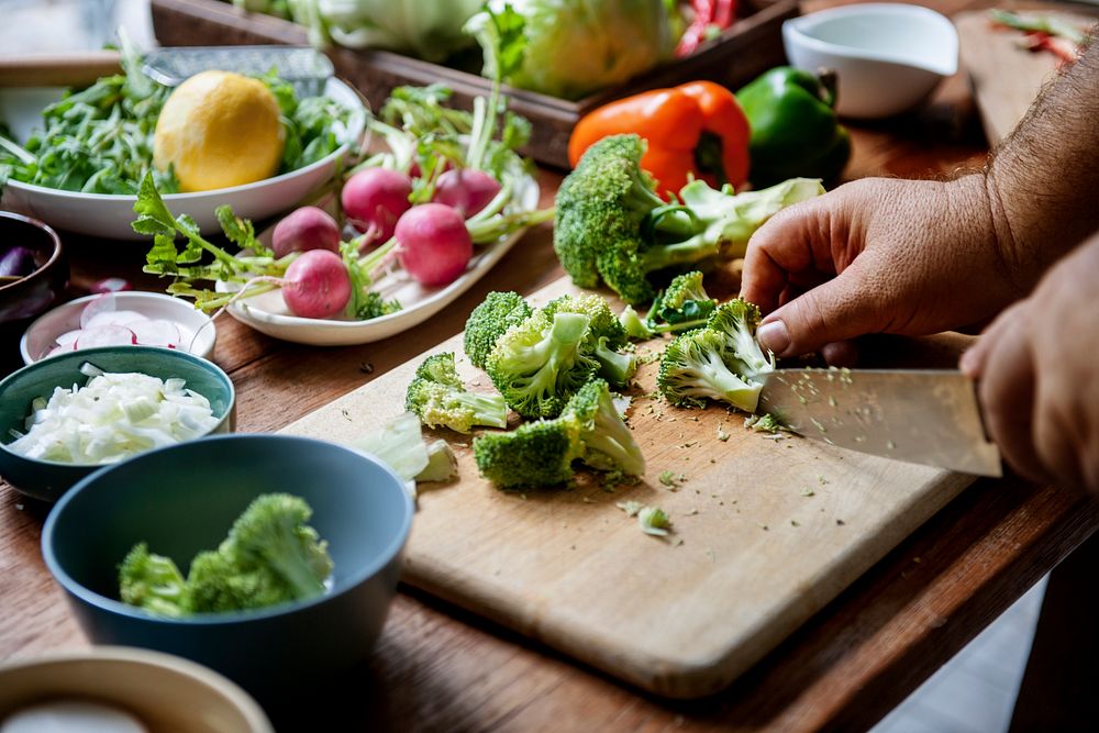 Closeup of hands with knife cutting broccoli on cut board