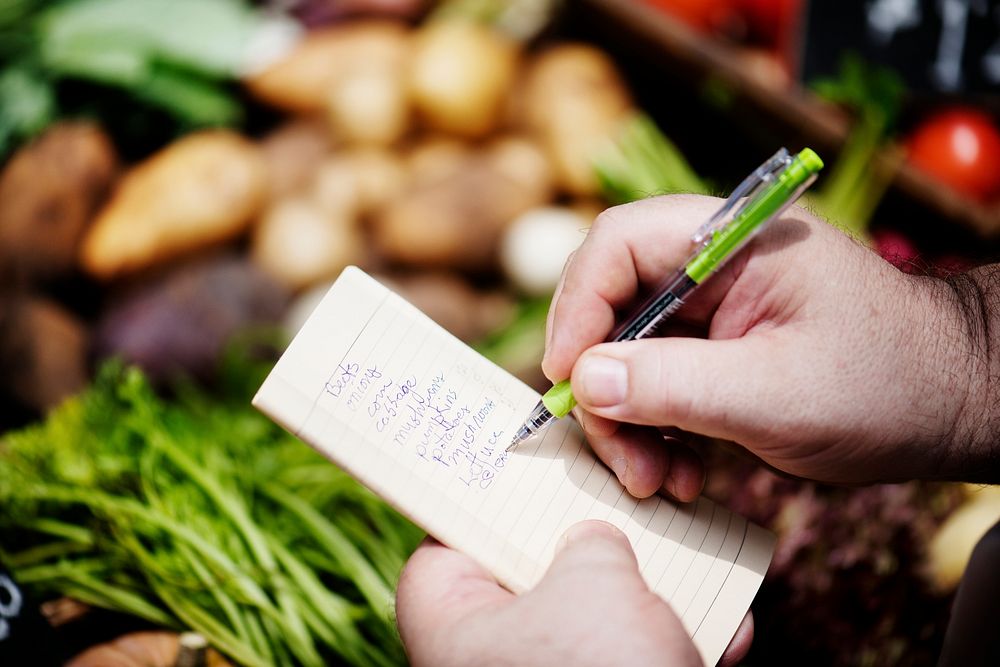 Closeup of hands writing vegetable list on notebook