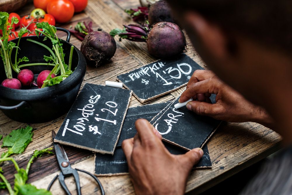 Rear view of man writing vegetable price on chalk board
