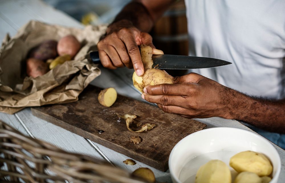Closeup of hand with knife peeling potato skin