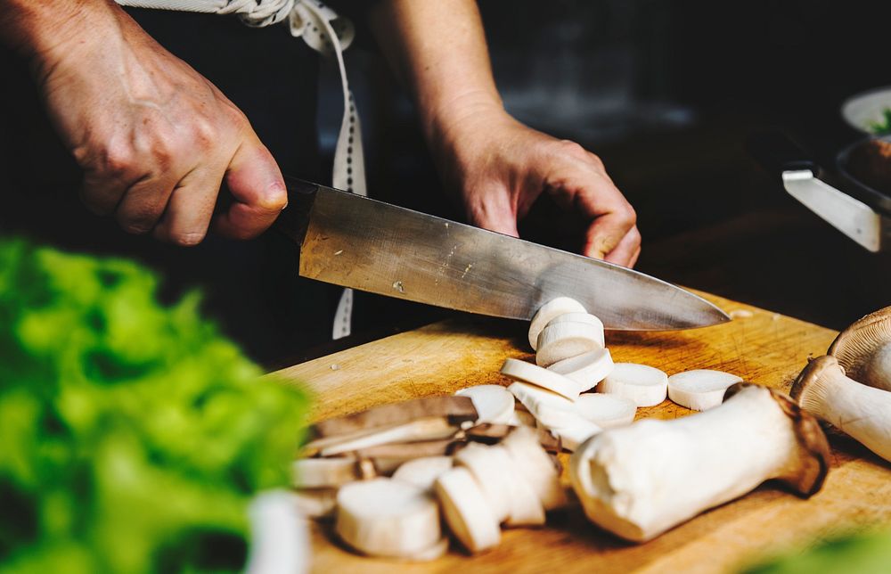 Closeup of hand with knife cutting mushroom