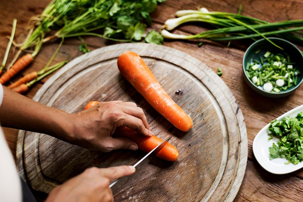 Hands chopping carrot and vegetable on wooden board