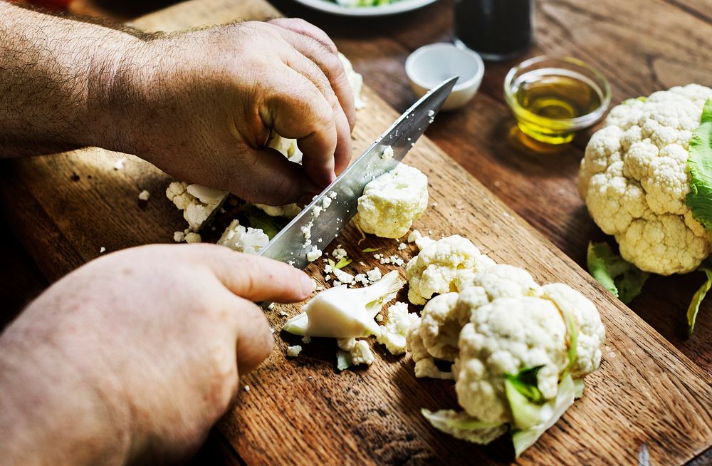 Closeup of hands with knife cutting fresh organic cauliflower