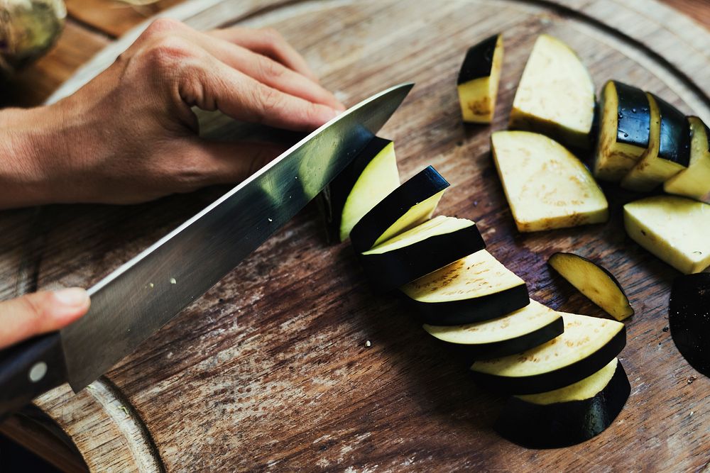 Hands chopping eggplant on wooden cutting board