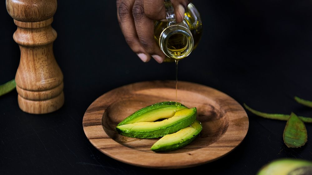 Closeup of fresh avocado on wooden plate topping with olive oil