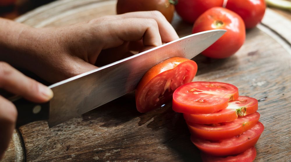 Hands holding a knife slicing a tomato