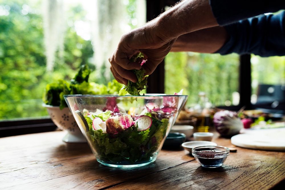 Hands mixing salad in a glass bowl