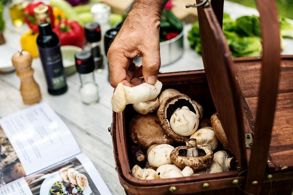 Closeup of hand picking up fresh mushrooms from wooden basket