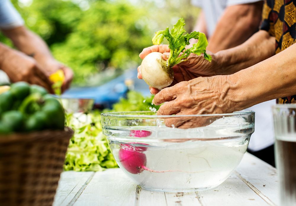Closeup of hands washing fresh white radish in glass water bowl
