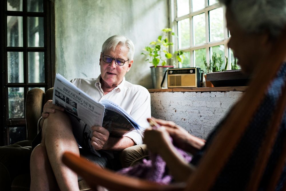 Senior man sitting on the couch reading newspaper