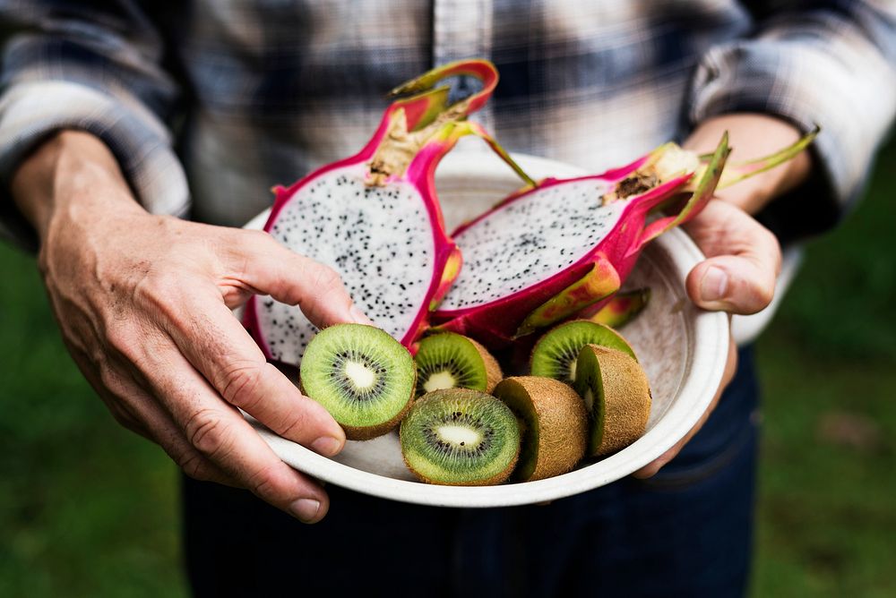 Closeup of hands holding bowl with cut dragon fruits and kiwi inside