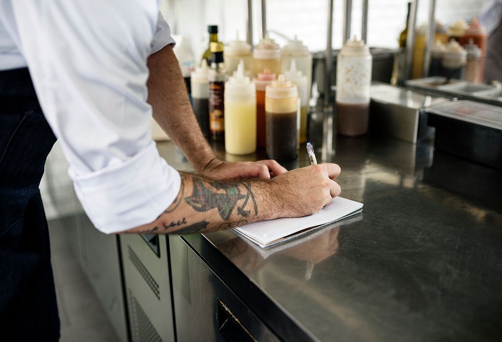 Hand with tattoo writing down an invetory in the kitchen