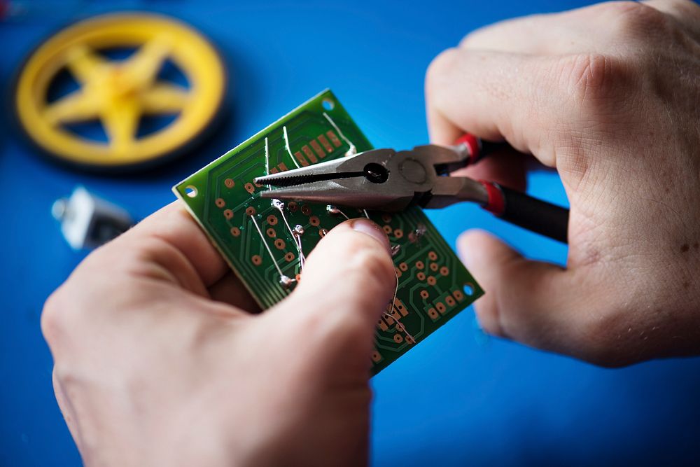 Closeup of hands with pliers and computer circuit mainboard