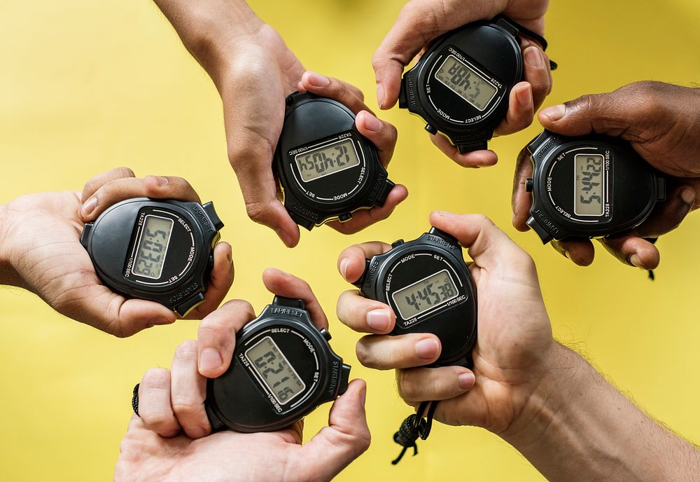 Closeup of hands holding stop watches with yellow background