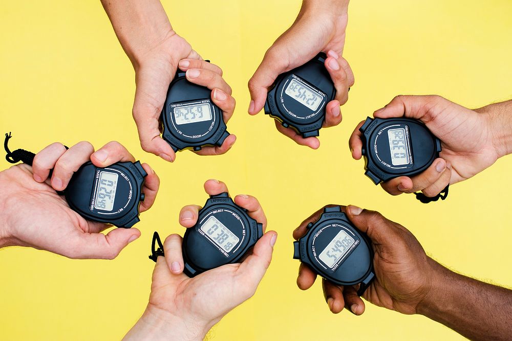 Closeup of hands holding stop watches with yellow background