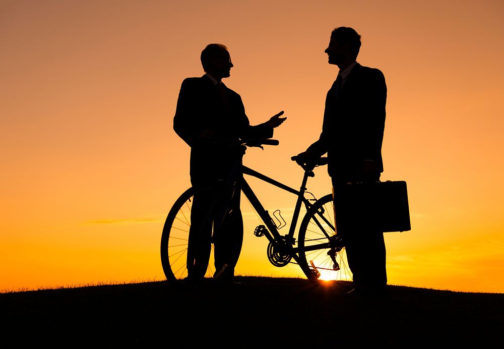 Businessmans are talking to each other with bicycle, one is holding the bicycle, one is holding the suitcase