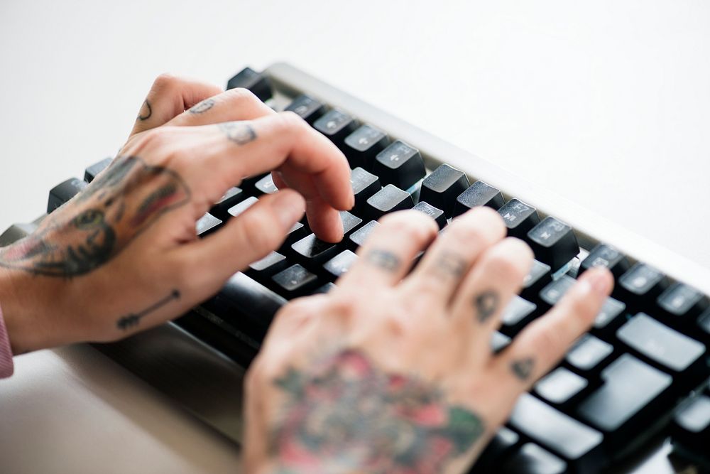 Hands with tattoo typing on a keyboard