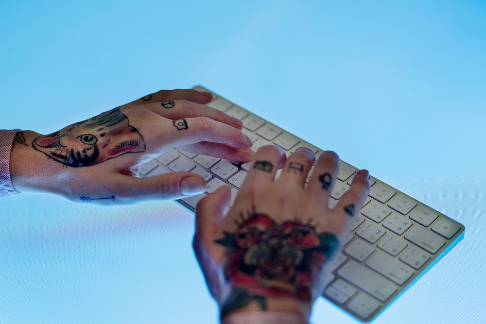 Hands with tattoo typing on a keyboard