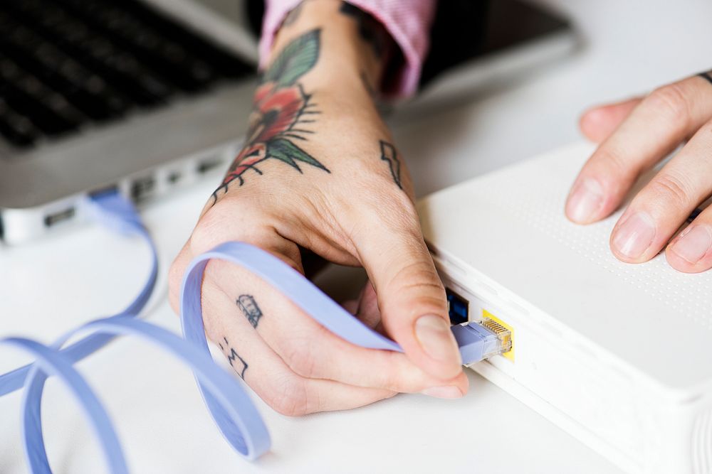Hands with tattoo holding LAN cable conect to device