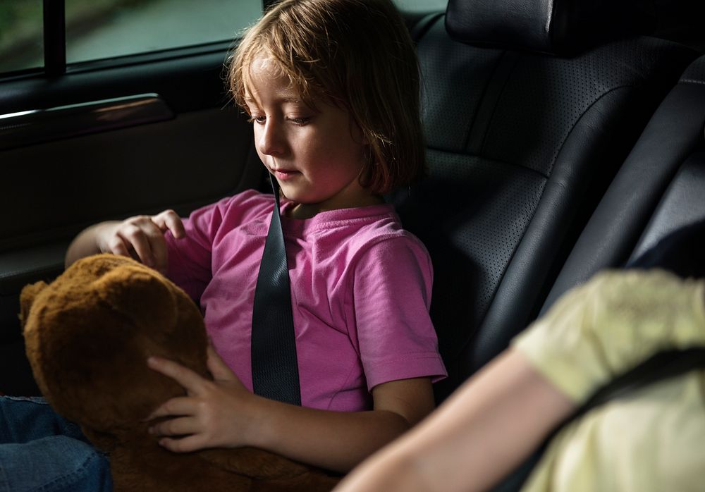 Young caucasian girl sitting inside the car playing with teddy bear