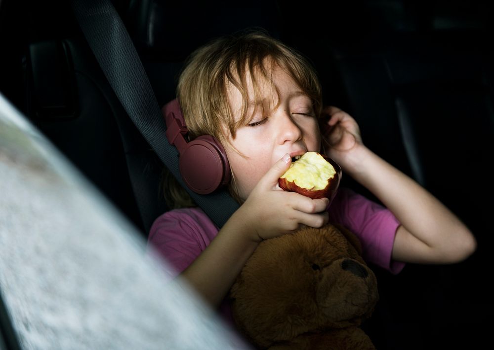 Closeup of young caucasian girl sitting inside the car eating apple