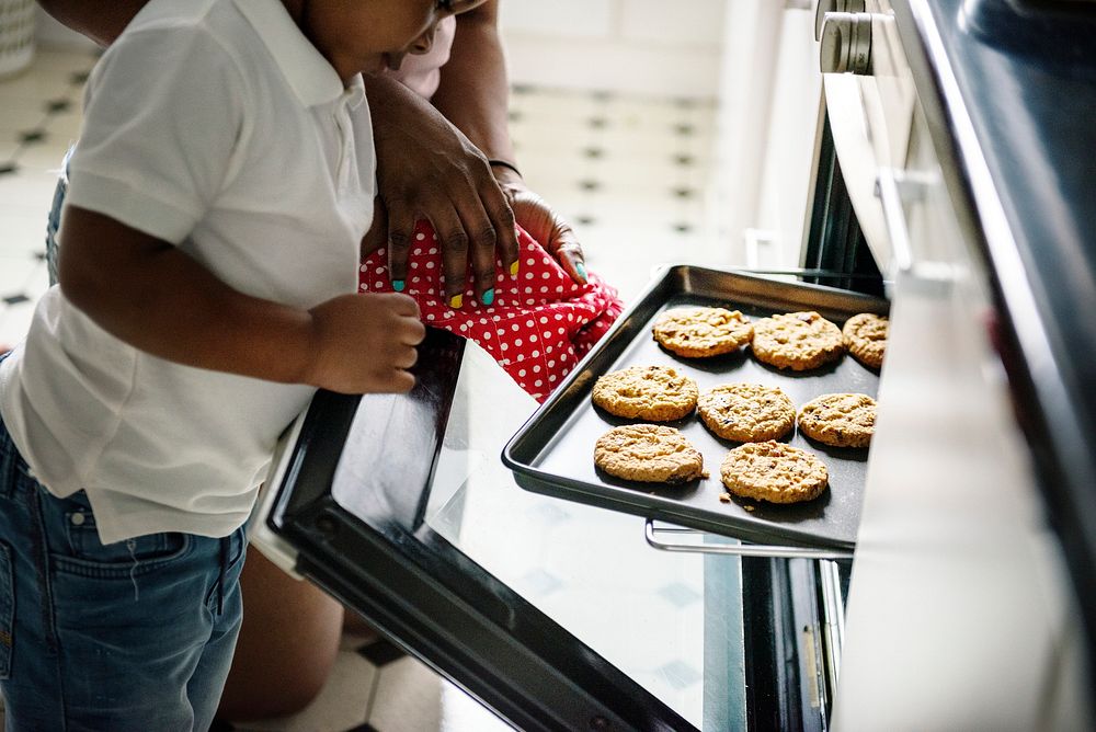 Black kid helping mom baking cookies in the kitchen