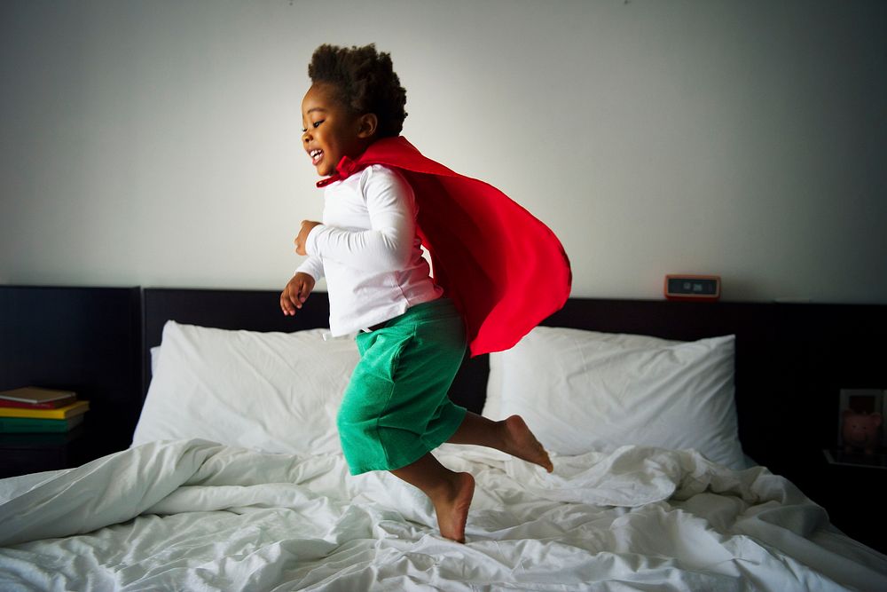 African descent kid jumping on the bed with robe