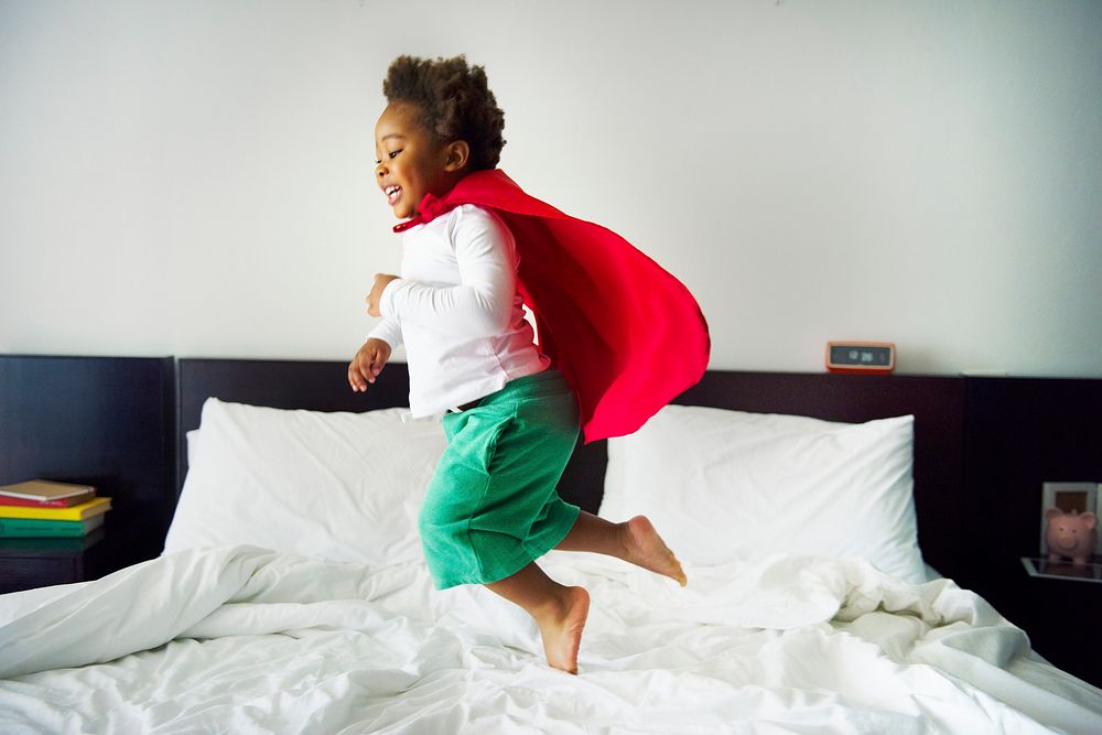 African descent kid jumping on the bed with robe