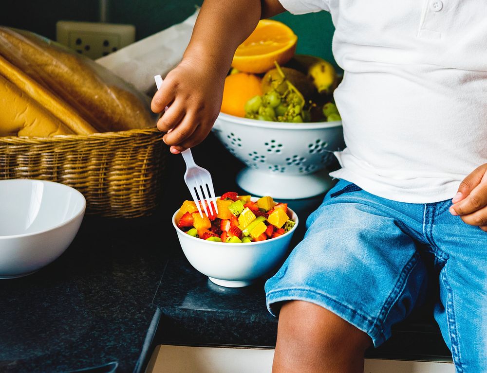 Black kid with fruit salad in the kitchen