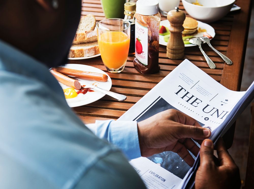 Rear view of black man reading newspaper while having breakfast