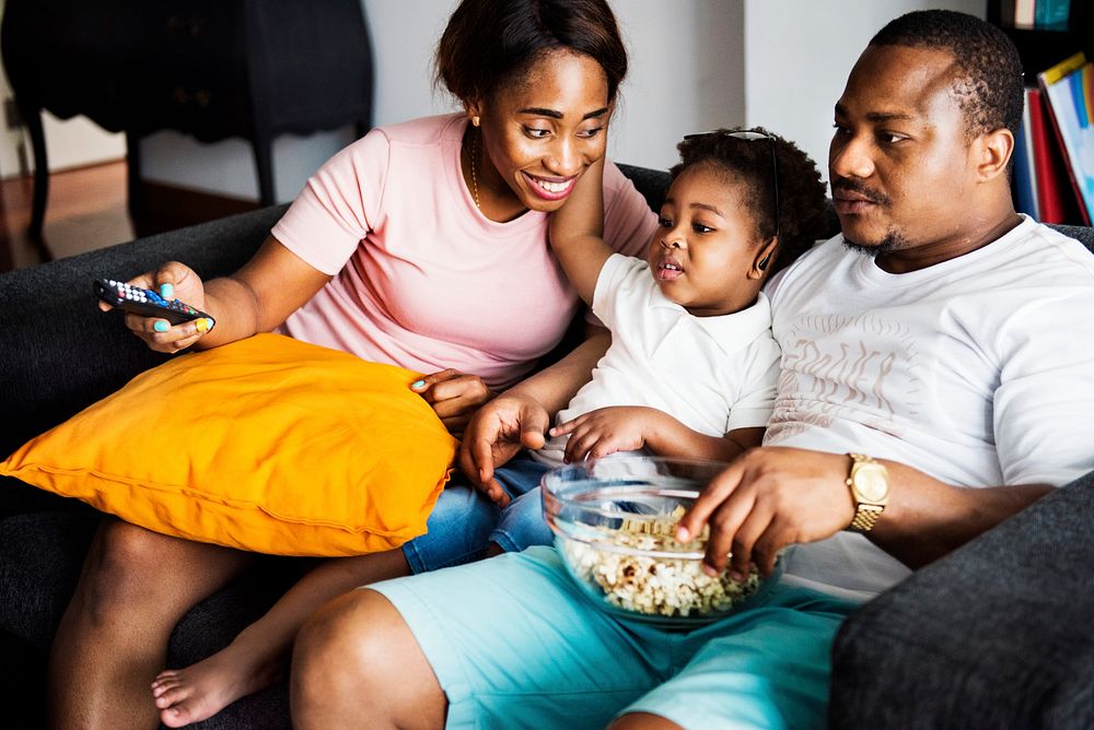 Black family eating popcorn while watching movie at home