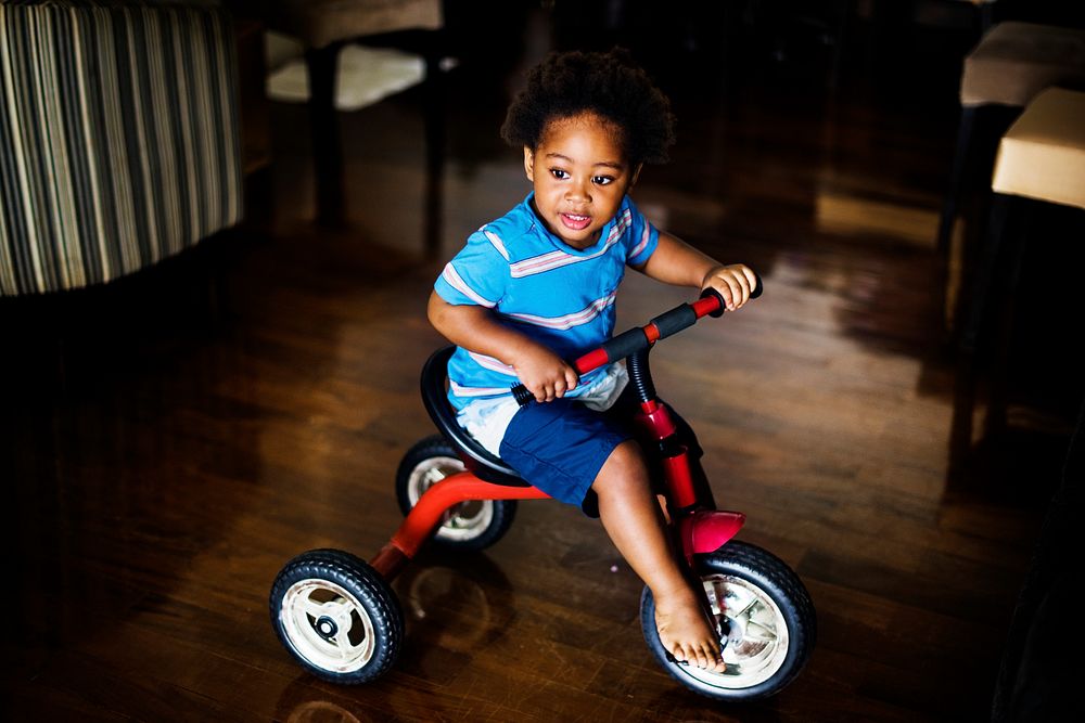 Black kid riding the bike in the house