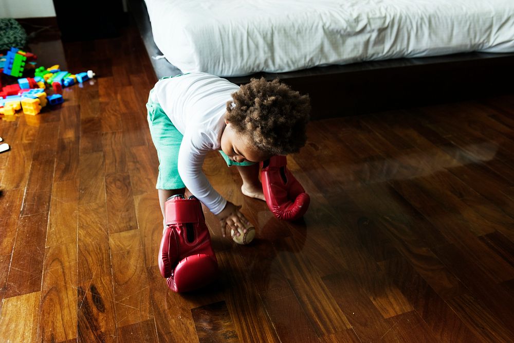 African descent kid with boxing glove on wooden floor