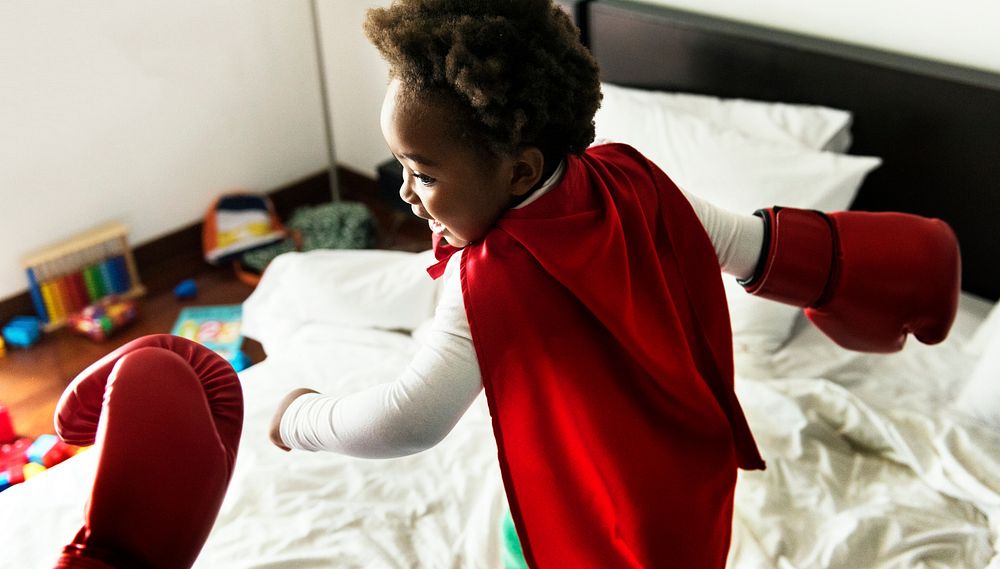 African descent kid wearing robe doing boxing with dad on the bed