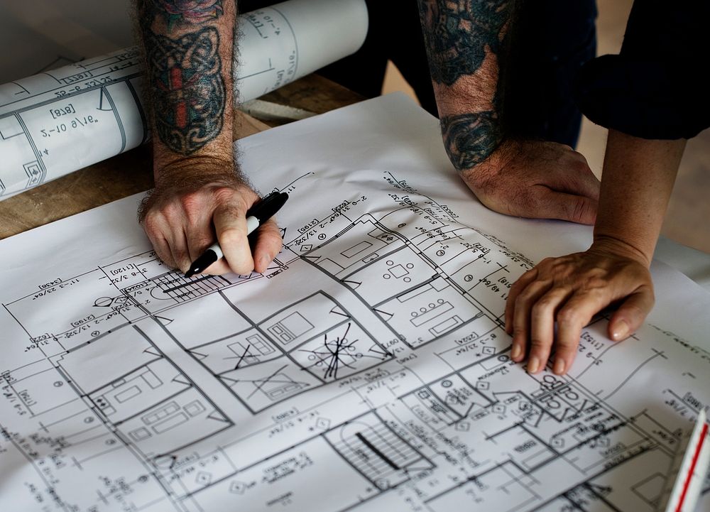 Hands with tattoo working on a blueprint
