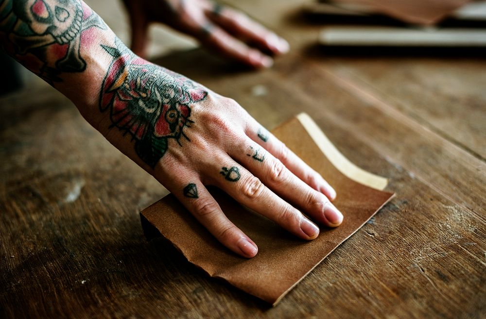 Hands with tattoo using sandpaper on a wood