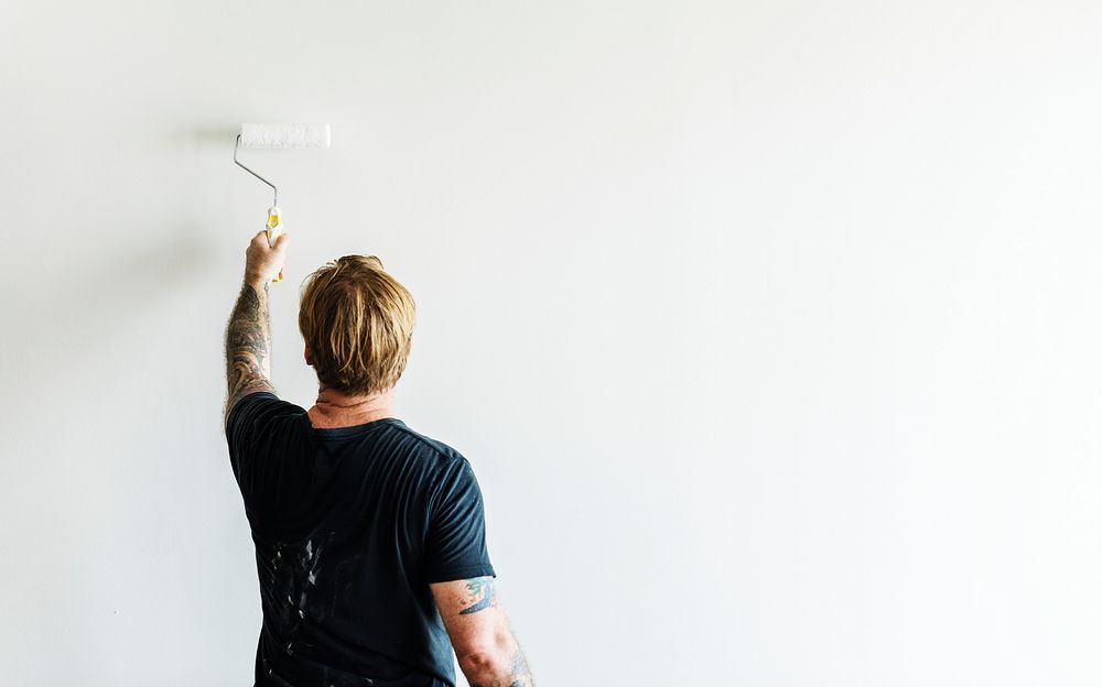 Man with tattoo holding roller paint the wall
