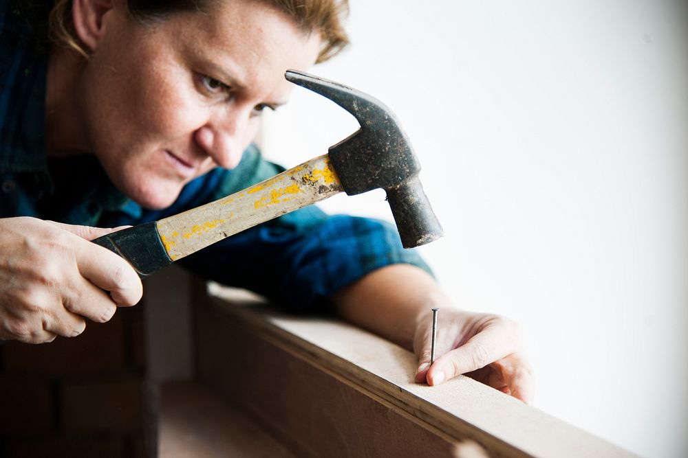 Woman carpenter using hammer pushing nail on a wood