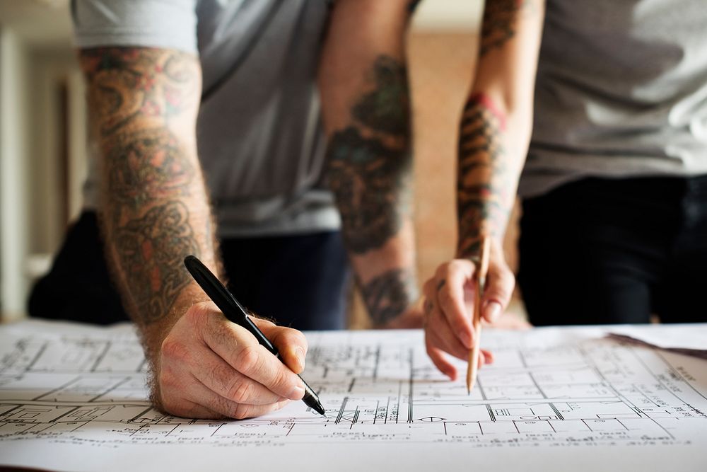 Hands with tattoo planning on a blueprint