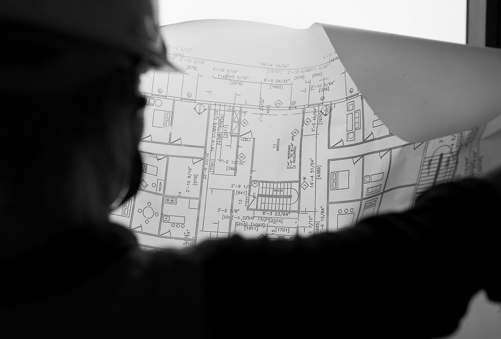 A worker with a hard helmet lokking to a blueprint