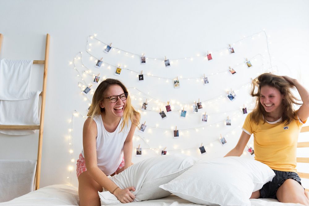 Women playing pillows fight on bed together