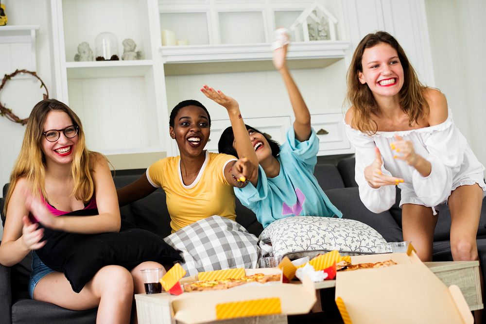 A group of diverse woman friends sitting on the couch eating pizza together