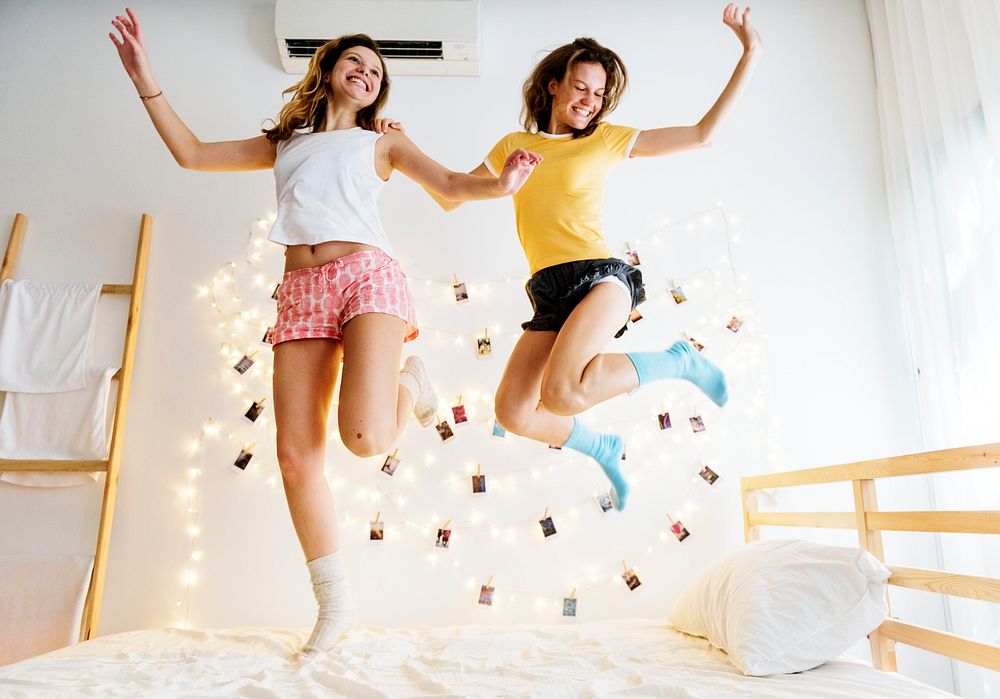 Two Caucasian women jumping on the bed together