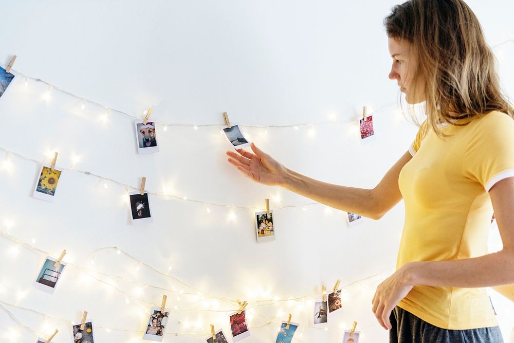 Woman looking at photos hanging with decoration lights on the white wall