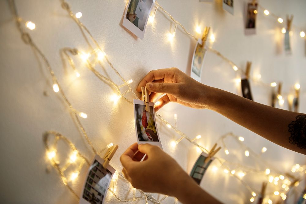 Closeup of habds with photos hanging with decoration lights on the white wall