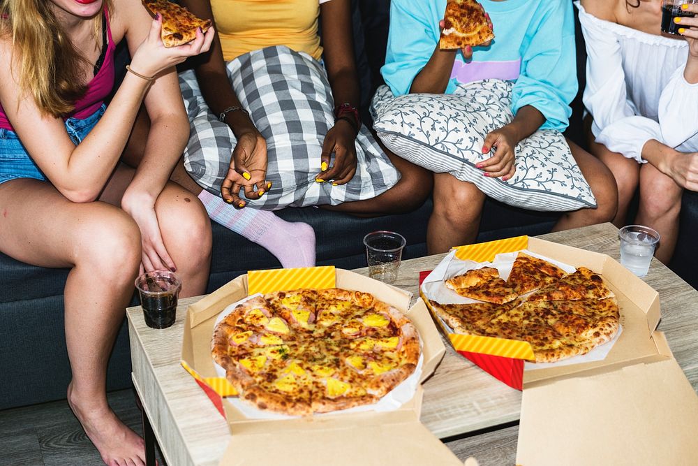 Diverse women sitting on the couch eating pizza together
