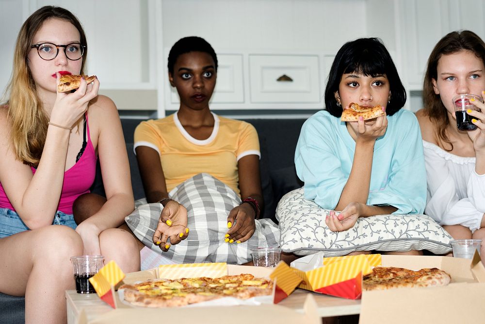 A group of diverse women sitting on the couch and eating pizza together