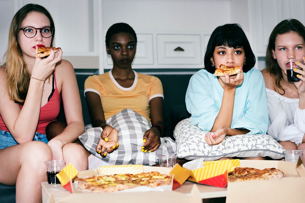 A diverse group of women sitting on the couch and eating pizza together